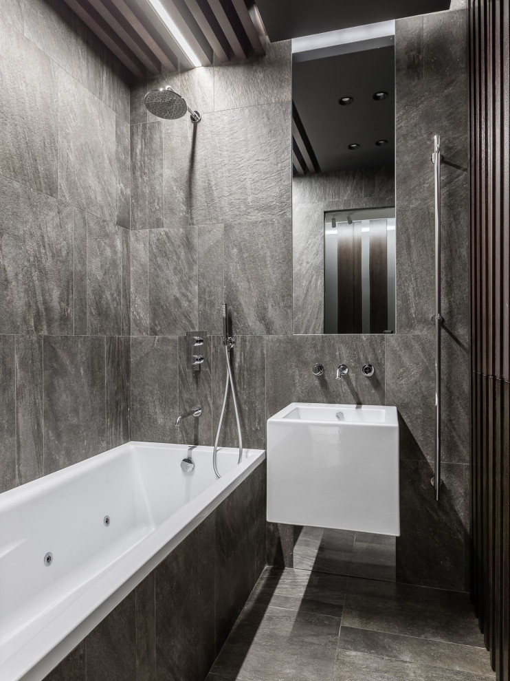 Modern inredning av ett badrum, med en dusch/badkar-kombination, grå kakel, grå väggar, ett väggmonterat handfat, grått golv och med dusch som är öppen