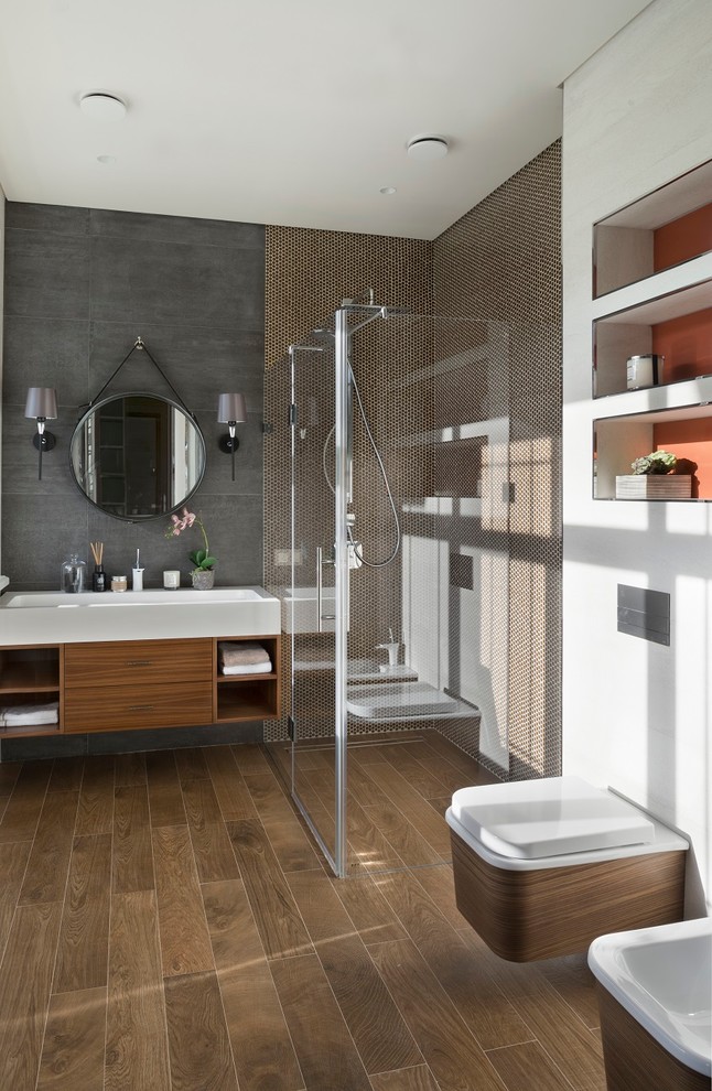 Aménagement d'une salle de bain contemporaine en bois brun avec un placard à porte plane, une douche à l'italienne, WC suspendus, un carrelage beige, un carrelage gris, un lavabo intégré et une cabine de douche à porte battante.