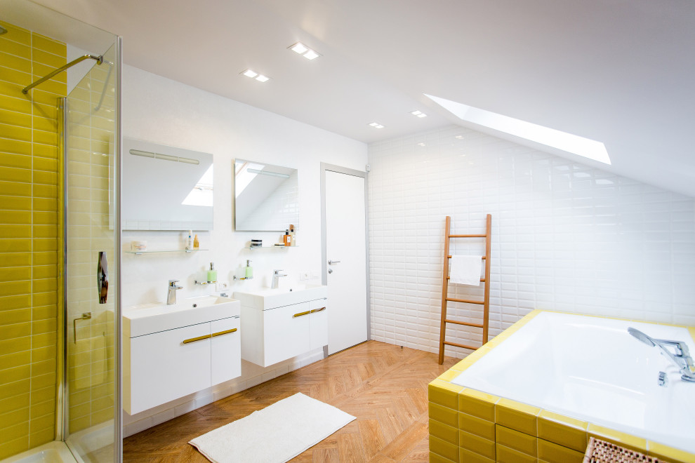 Modernes Badezimmer mit weißer Wandfarbe, braunem Holzboden, braunem Boden, flächenbündigen Schrankfronten, weißen Schränken, Einbaubadewanne, weißen Fliesen, gelben Fliesen, Metrofliesen und Waschtischkonsole in Sonstige