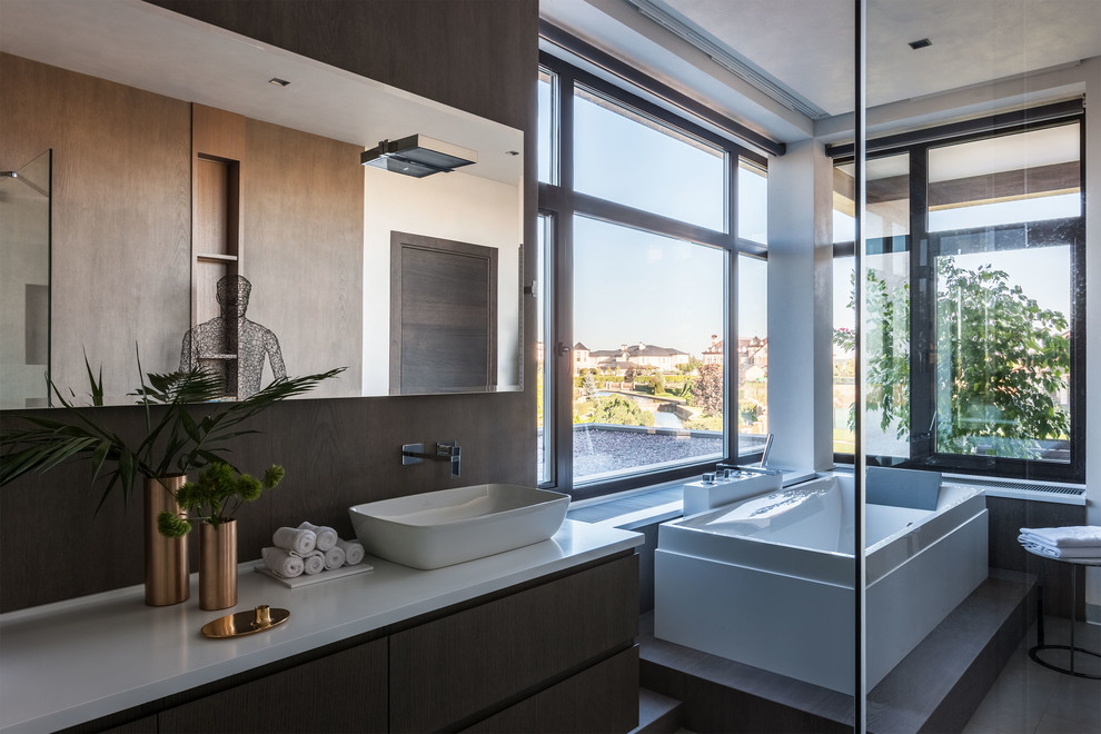 На фото: главная ванная комната в современном стиле с отдельно стоящей ванной, настольной раковиной, темными деревянными фасадами и белой столешницей