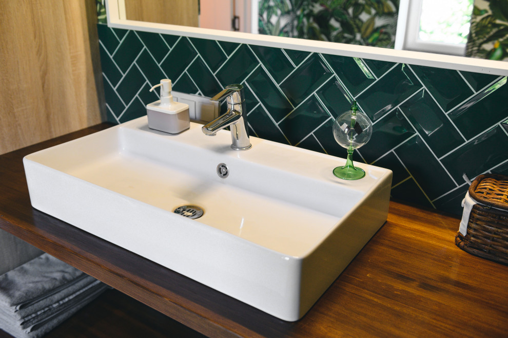 Modern inredning av ett litet brun brunt badrum med dusch, med bruna skåp, en dusch i en alkov, en toalettstol med hel cisternkåpa, grön kakel, porslinskakel, gröna väggar, klinkergolv i porslin, ett nedsänkt handfat, träbänkskiva, beiget golv och dusch med gångjärnsdörr