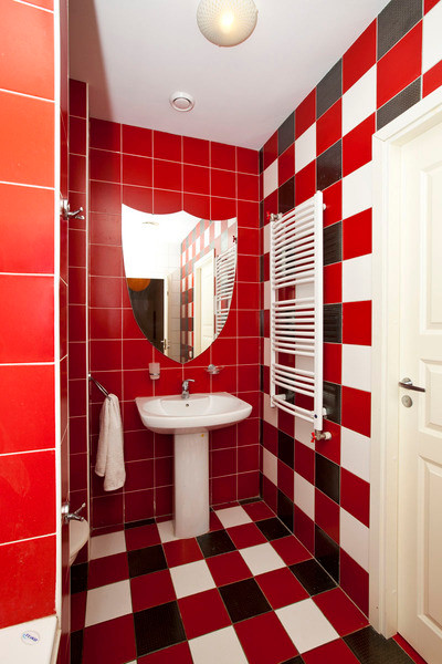 Modelo de cuarto de baño infantil de tamaño medio con sanitario de una pieza, baldosas y/o azulejos rojos, paredes multicolor y suelo de baldosas de cerámica