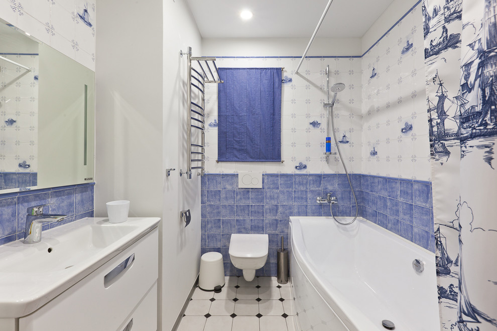 Idéer för ett mellanstort maritimt badrum, med en dusch/badkar-kombination, en vägghängd toalettstol, keramikplattor, vita väggar, klinkergolv i porslin, släta luckor, vita skåp, ett badkar i en alkov, blå kakel, vit kakel, ett integrerad handfat och dusch med duschdraperi