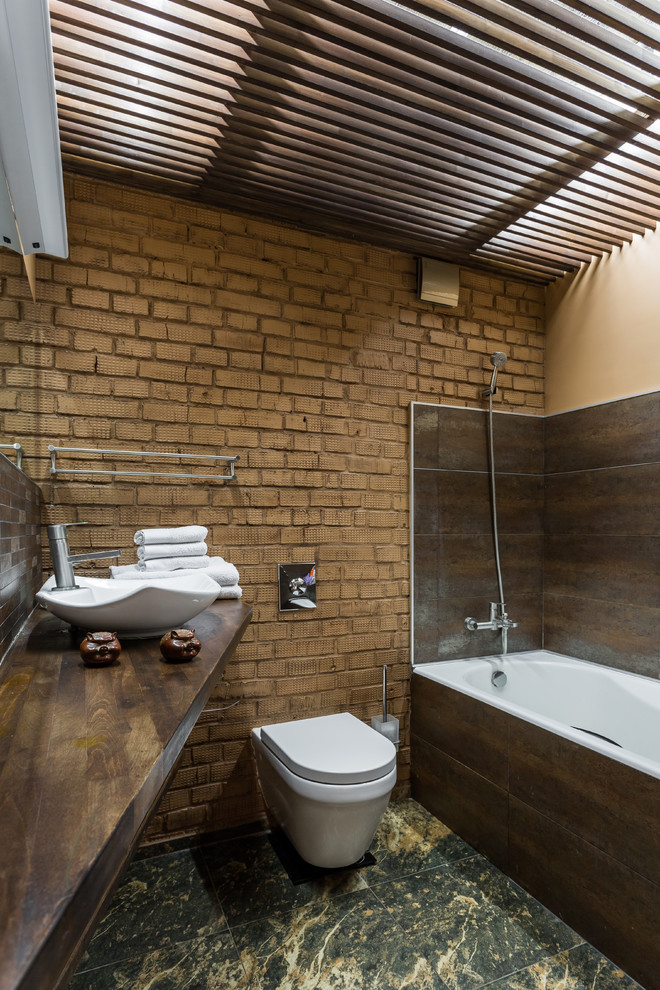 Photo of an urban ensuite bathroom in Moscow with a wall mounted toilet, brown walls, a vessel sink and brown tiles.