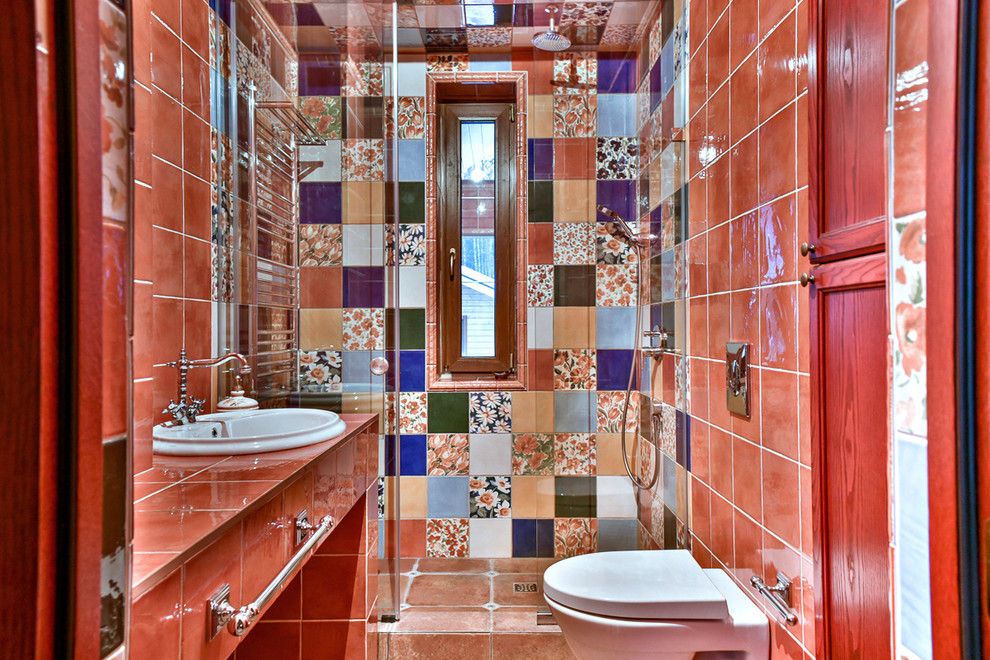 Diseño de cuarto de baño campestre con ducha abierta, sanitario de pared, aseo y ducha, ducha con puerta con bisagras, baldosas y/o azulejos rojos y baldosas y/o azulejos multicolor