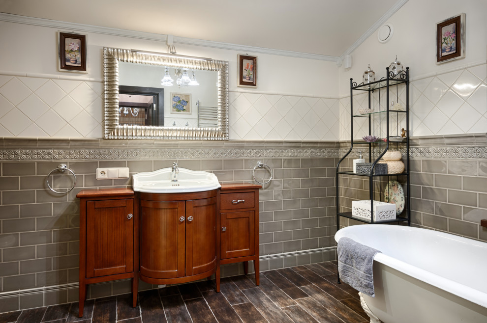 Imagen de cuarto de baño principal clásico renovado con puertas de armario de madera oscura, bañera con patas, baldosas y/o azulejos grises, paredes blancas, lavabo encastrado, suelo marrón y encimeras marrones