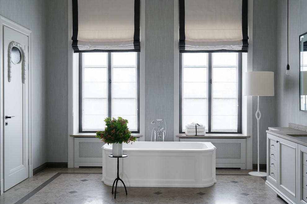 Imagen de cuarto de baño principal tradicional renovado con bañera exenta, armarios con paneles empotrados, paredes grises, lavabo bajoencimera, puertas de armario grises y suelo beige