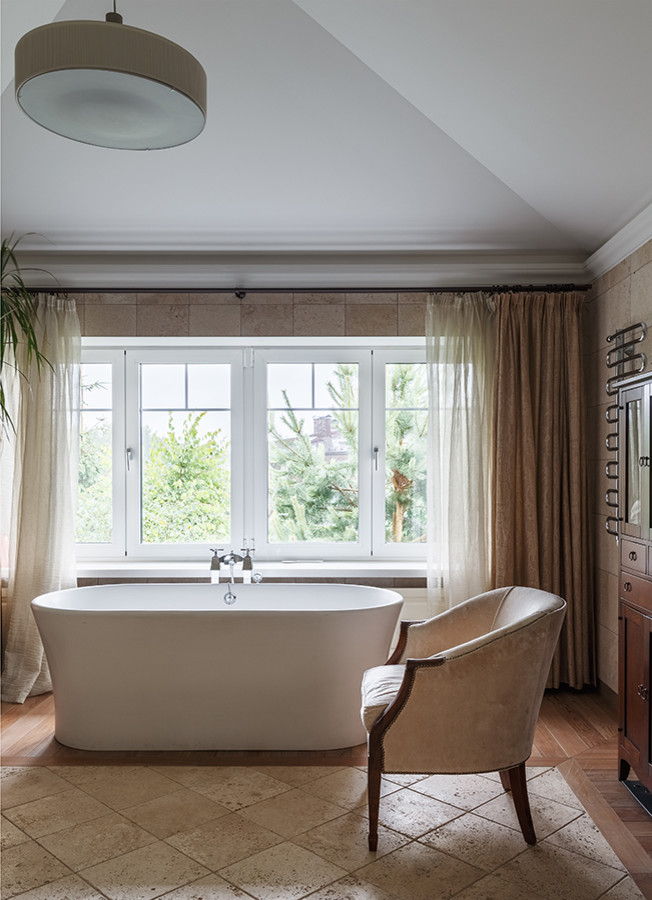 На фото: главная ванная комната в стиле неоклассика (современная классика) с отдельно стоящей ванной, коричневым полом и акцентной стеной с