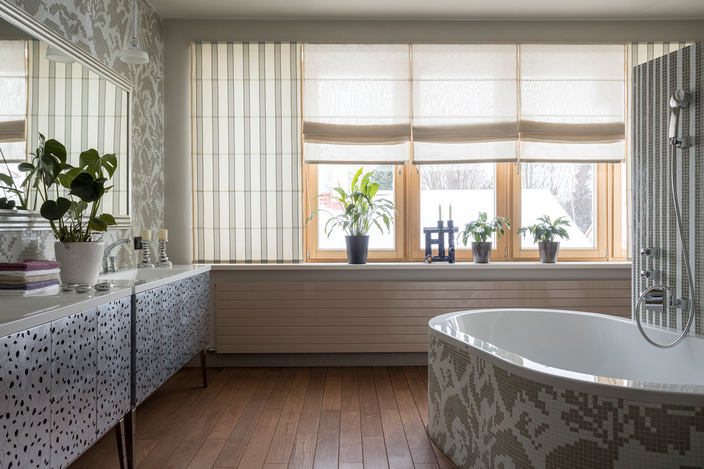 Inredning av ett modernt stort vit vitt en-suite badrum, med grå skåp, grå väggar, mörkt trägolv, brunt golv, släta luckor, ett fristående badkar, bänkskiva i akrylsten, ett integrerad handfat, en dusch/badkar-kombination och med dusch som är öppen