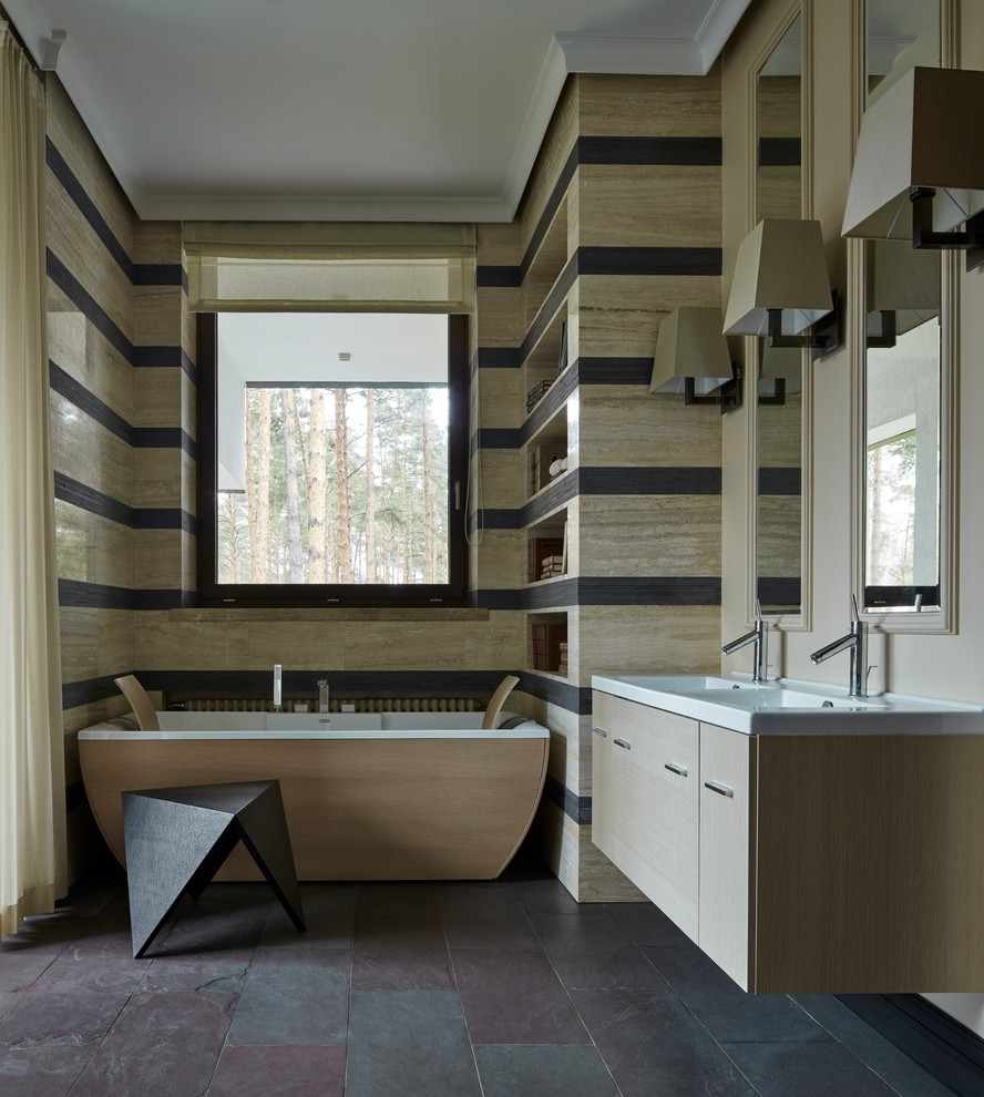 На фото: главная ванная комната в современном стиле с плоскими фасадами, светлыми деревянными фасадами, отдельно стоящей ванной и раковиной с несколькими смесителями с
