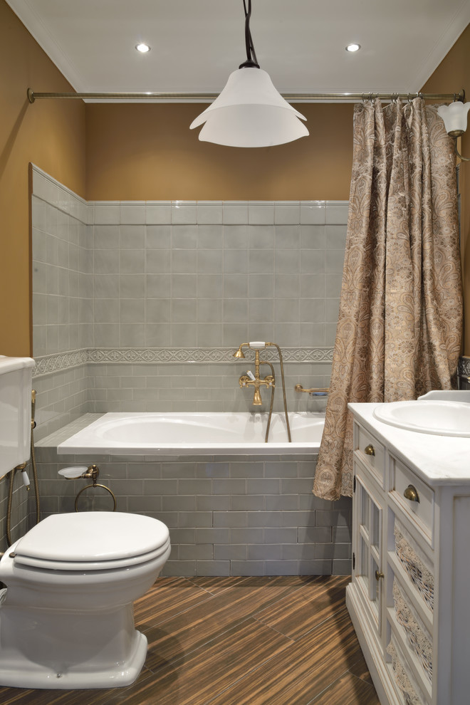 Foto på ett vintage vit en-suite badrum, med luckor med infälld panel, vita skåp, ett badkar i en alkov, en dusch/badkar-kombination, en toalettstol med separat cisternkåpa, grå kakel, bruna väggar, ett nedsänkt handfat, brunt golv och dusch med duschdraperi