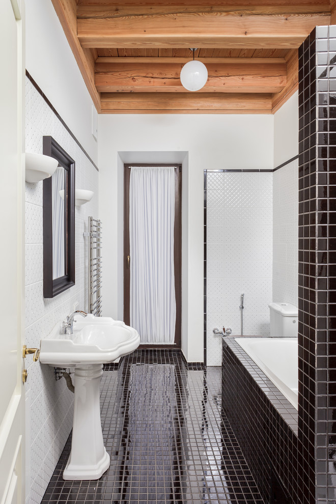 Diseño de cuarto de baño clásico con lavabo con pedestal, bañera encastrada, sanitario de dos piezas, baldosas y/o azulejos blancos, paredes blancas y suelo con mosaicos de baldosas