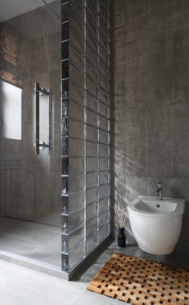 Modelo de cuarto de baño actual con sanitario de pared, baldosas y/o azulejos grises, paredes grises y aseo y ducha