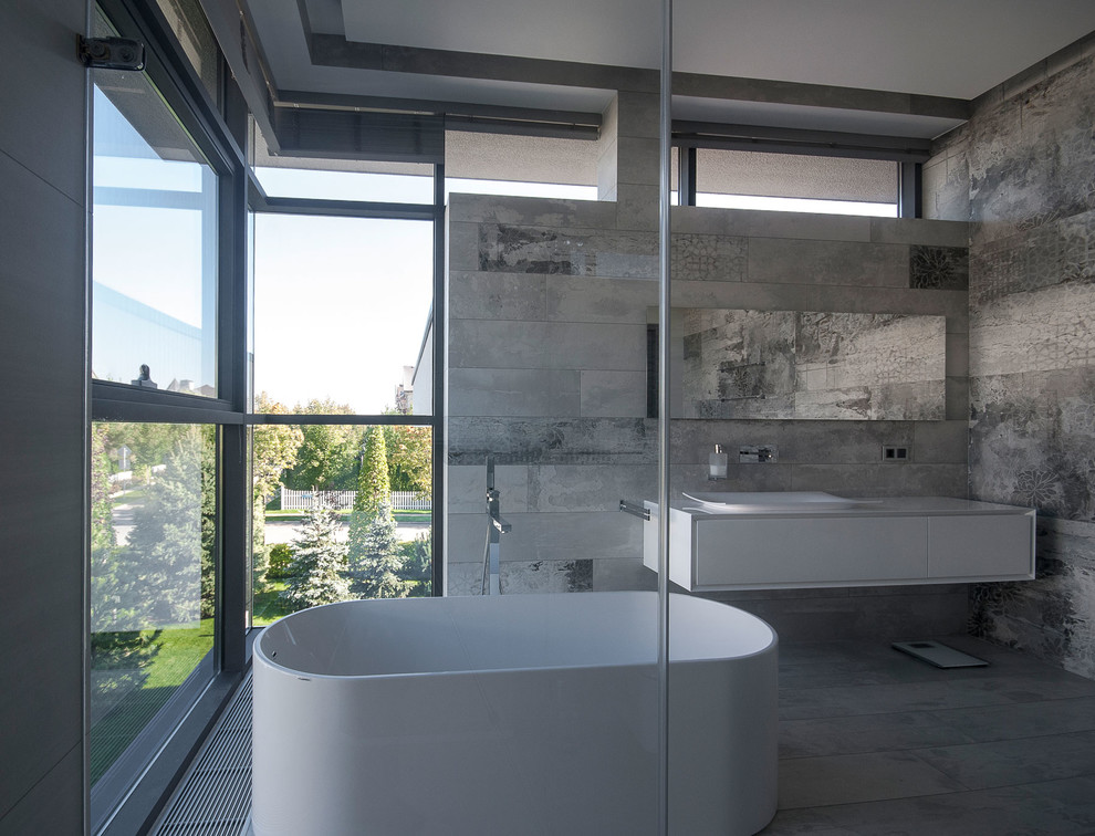Exemple d'une salle de bain principale tendance avec un placard à porte plane, des portes de placard blanches, une baignoire indépendante, un carrelage gris et une vasque.