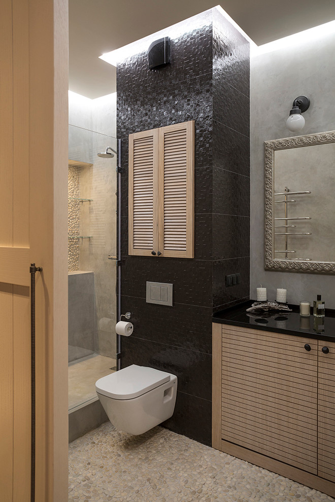 Modern inredning av ett mellanstort badrum med dusch, med skåp i ljust trä, en vägghängd toalettstol, grå väggar, klinkergolv i småsten, ett integrerad handfat, bänkskiva i kvarts, släta luckor, en dusch i en alkov och svart kakel