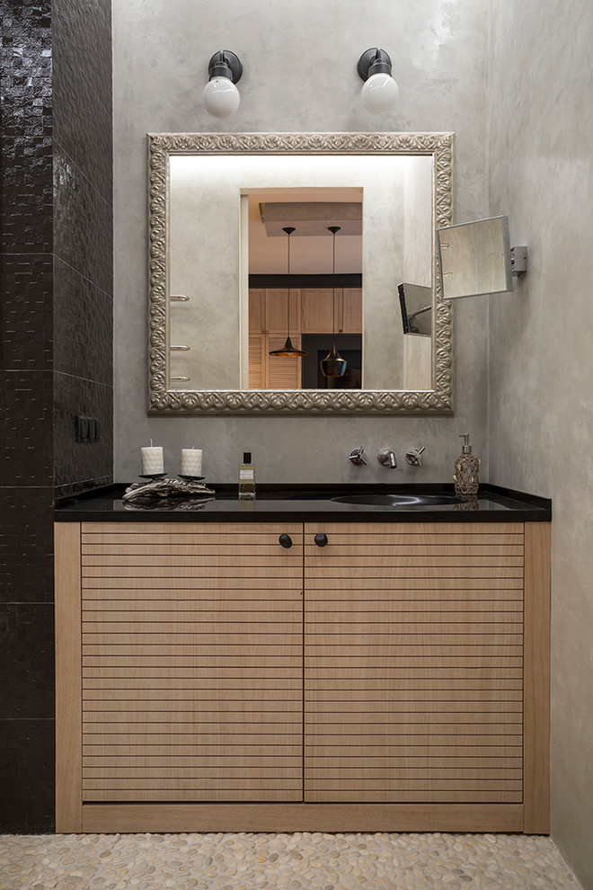 Cette image montre une salle d'eau design en bois clair de taille moyenne avec un mur gris, un sol en galet, un lavabo intégré, un plan de toilette en quartz modifié, un placard à porte plane et un carrelage noir.