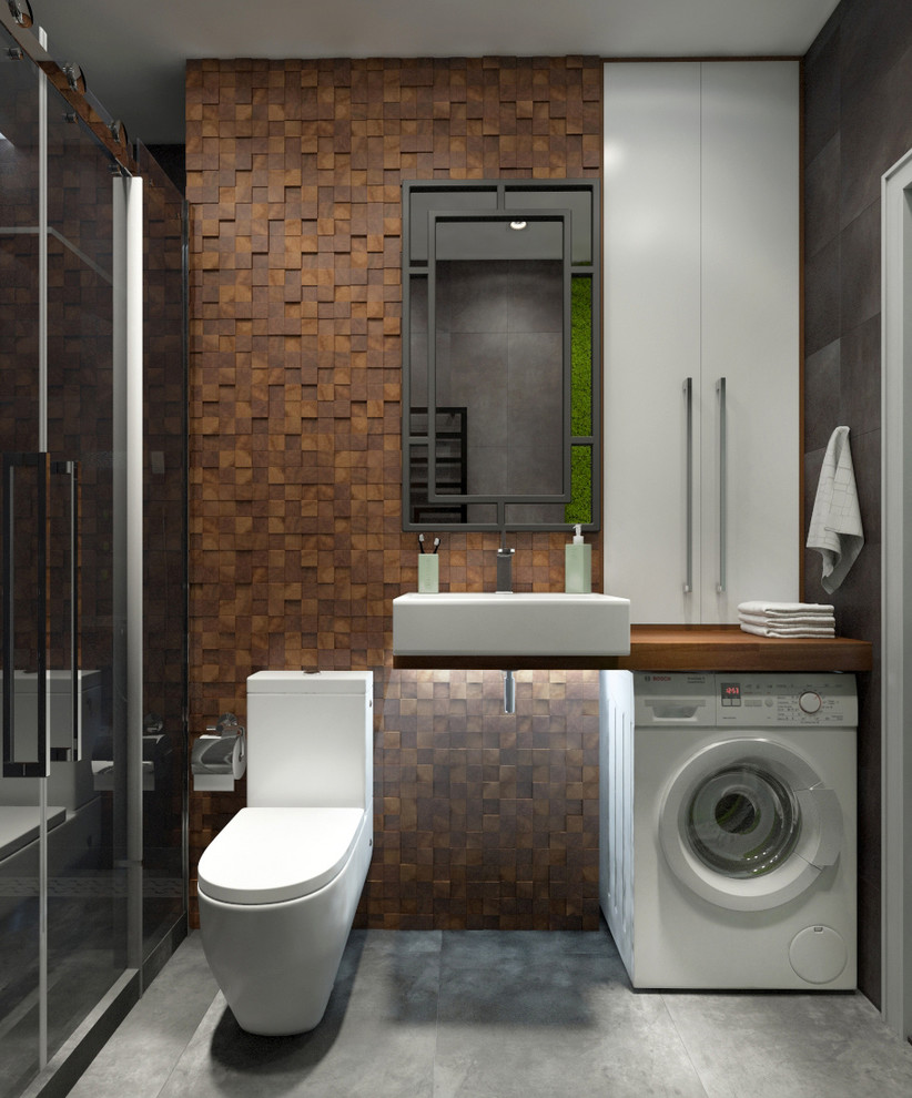 This is an example of a medium sized contemporary bathroom in Moscow with flat-panel cabinets, a one-piece toilet, brown tiles, ceramic tiles, brown walls, porcelain flooring, a vessel sink, wooden worktops, grey floors, a sliding door and brown worktops.