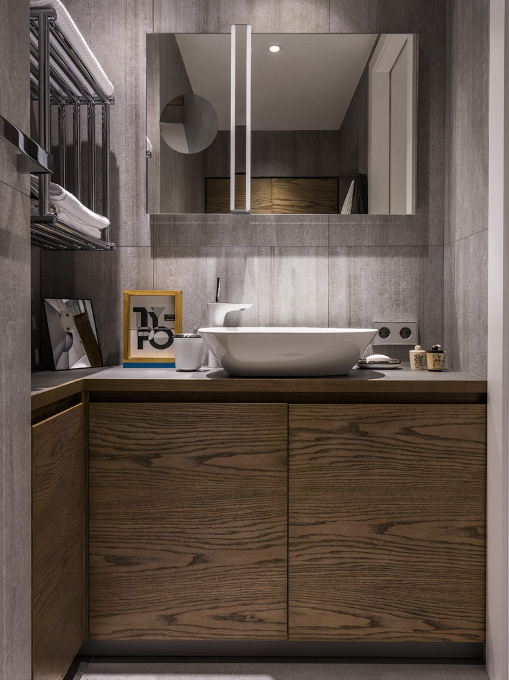 На фото: ванная комната в современном стиле с плоскими фасадами, темными деревянными фасадами, серой плиткой и настольной раковиной с