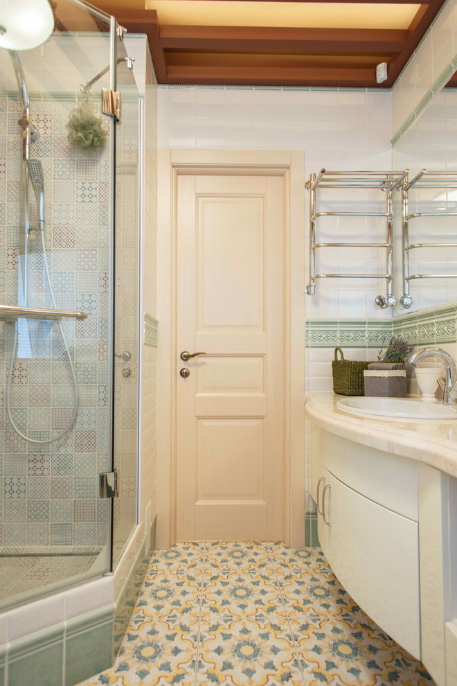 Cette image montre une salle de bain traditionnelle avec un placard à porte plane, des portes de placard blanches, un mur blanc, un sol en carrelage de céramique, un lavabo posé, un carrelage multicolore et une cabine de douche à porte battante.