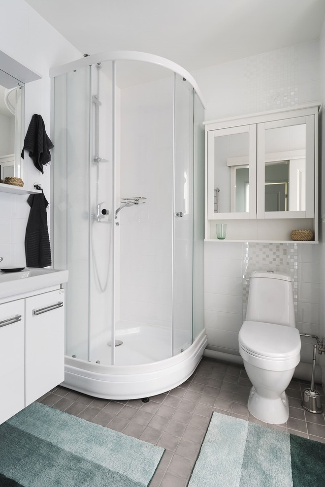 Photo of a medium sized scandinavian shower room bathroom in Saint Petersburg with flat-panel cabinets, white cabinets, a corner shower, a one-piece toilet, white tiles, ceramic tiles, white walls, porcelain flooring, a built-in sink, grey floors, a sliding door and a feature wall.