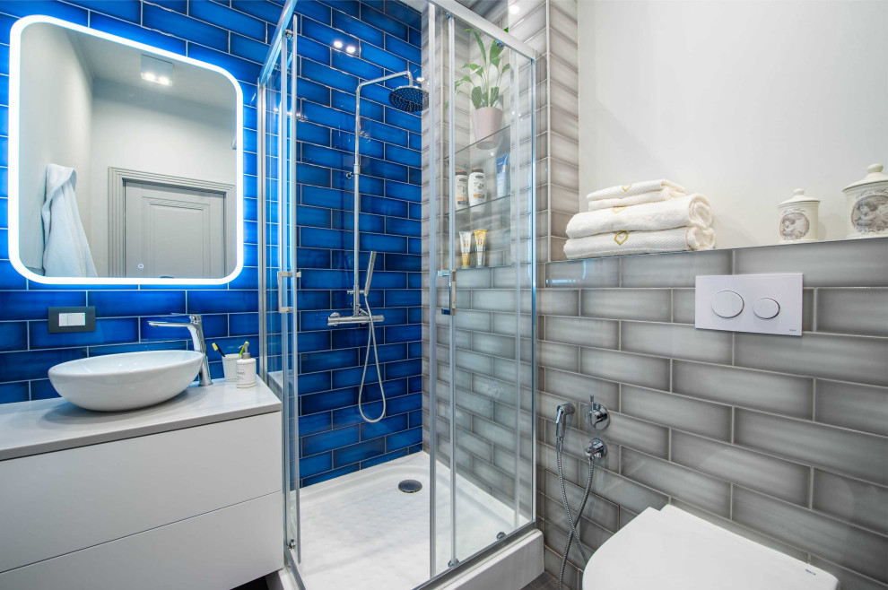 Свежая идея для дизайна: маленькая ванная комната в скандинавском стиле с плоскими фасадами, серыми фасадами, угловым душем, инсталляцией, разноцветной плиткой, керамической плиткой, серыми стенами, полом из керамогранита, душевой кабиной, накладной раковиной, столешницей из искусственного камня, серым полом, душем с раздвижными дверями, серой столешницей, нишей, тумбой под одну раковину и подвесной тумбой для на участке и в саду - отличное фото интерьера
