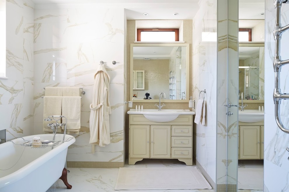 На фото: главная ванная комната в стиле неоклассика (современная классика) с фасадами с выступающей филенкой, бежевыми фасадами, ванной на ножках, белой плиткой и монолитной раковиной с