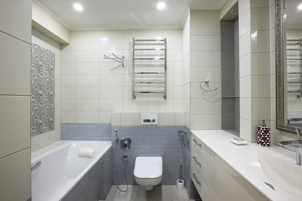 Immagine di una stanza da bagno design con ante bianche, vasca ad alcova, WC sospeso, piastrelle beige, piastrelle grigie e lavabo integrato