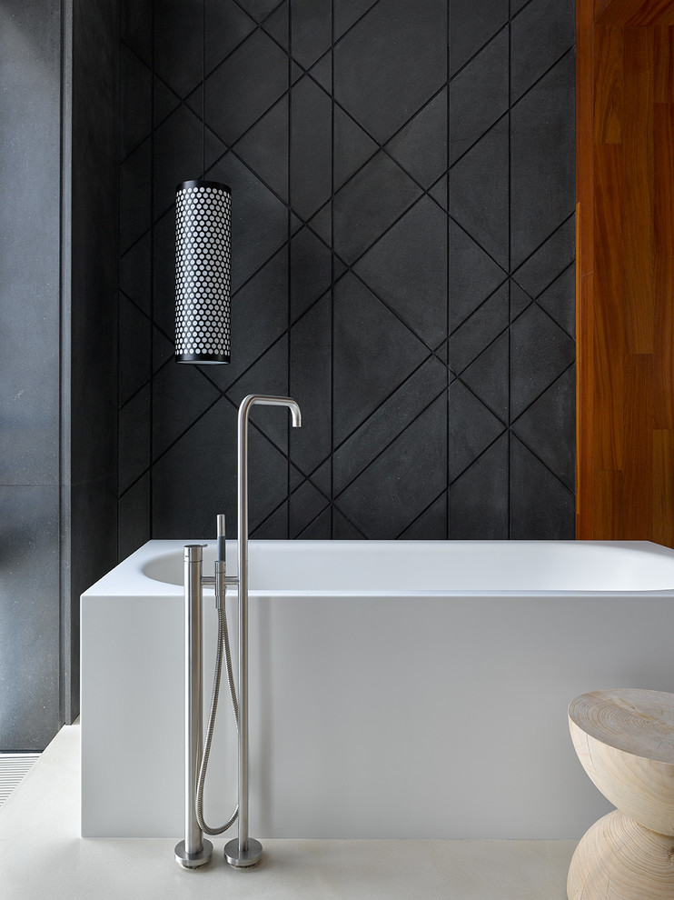 Modelo de cuarto de baño principal actual de tamaño medio con bañera exenta, baldosas y/o azulejos negros, suelo de cemento y suelo beige
