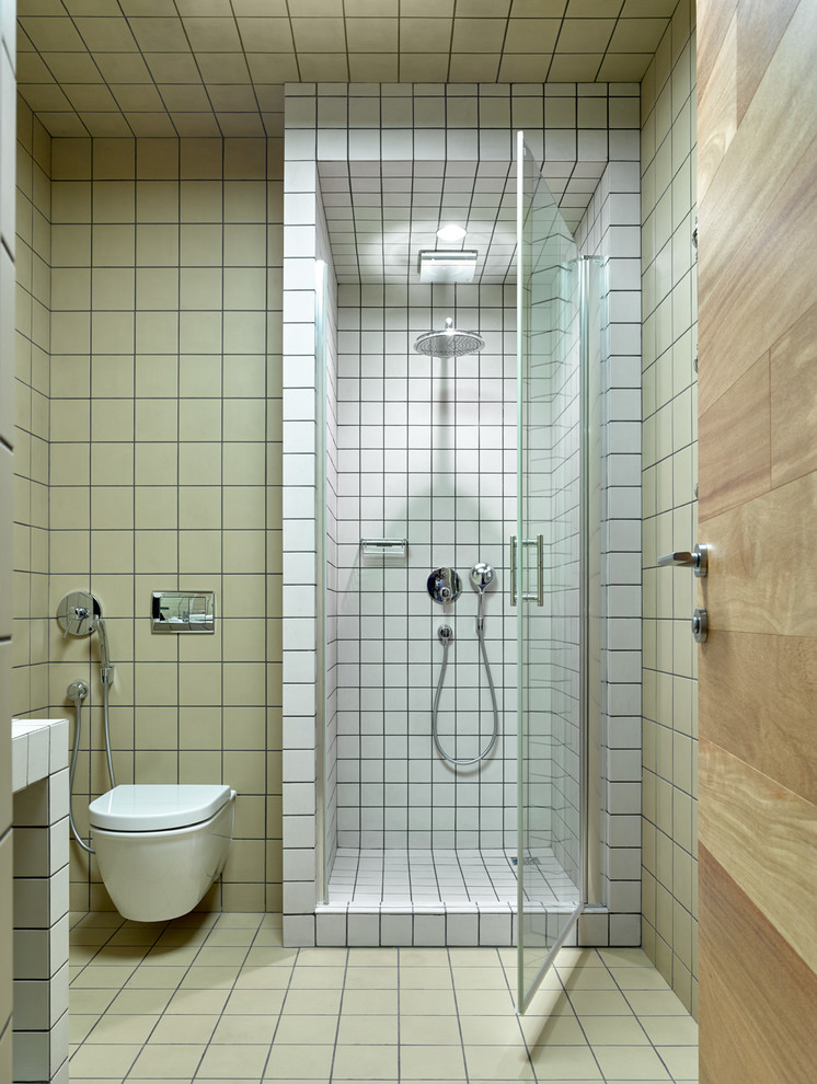 Exempel på ett litet minimalistiskt badrum med dusch, med en vägghängd toalettstol, cementgolv, kaklad bänkskiva, en dusch i en alkov, beige kakel, beige väggar, flerfärgat golv och dusch med gångjärnsdörr