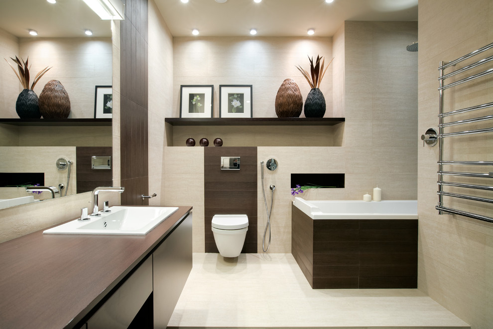 Пример оригинального дизайна: ванная комната среднего размера в современном стиле с плоскими фасадами, темными деревянными фасадами, ванной в нише, бежевой плиткой, керамогранитной плиткой, бежевыми стенами, полом из керамогранита, столешницей из дерева, инсталляцией, накладной раковиной и коричневой столешницей
