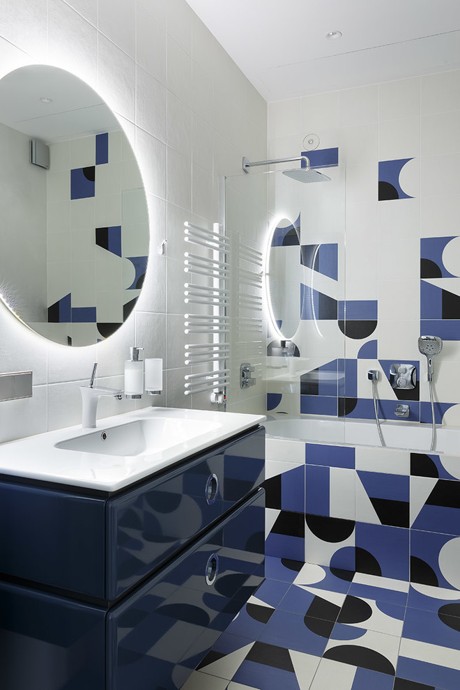 На фото: главная ванная комната в современном стиле с плоскими фасадами, синими фасадами, ванной в нише, душем над ванной, монолитной раковиной, разноцветным полом, белой столешницей, синей плиткой и белой плиткой с