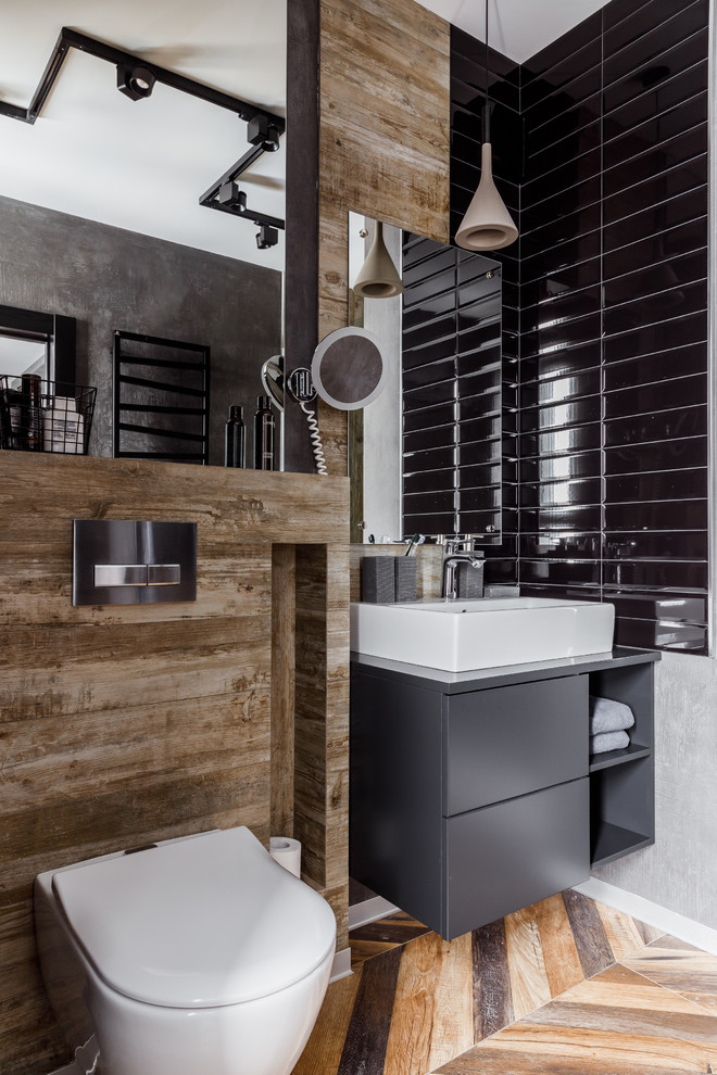 Foto på ett mellanstort industriellt grå badrum med dusch, med en vägghängd toalettstol, svart kakel, keramikplattor, grå väggar, klinkergolv i porslin, bänkskiva i akrylsten, brunt golv, släta luckor, grå skåp och ett fristående handfat