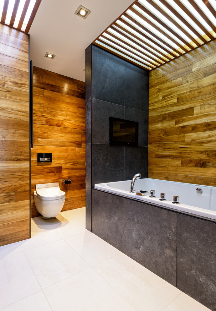 Cette image montre une salle de bain design avec une baignoire en alcôve, WC suspendus, un carrelage noir et un mur marron.