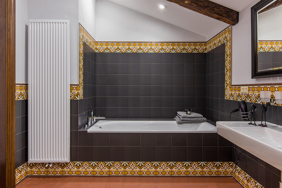 Klassisches Badezimmer En Suite mit Badewanne in Nische, schwarzen Fliesen, farbigen Fliesen, Wandwaschbecken und orangem Boden in Sonstige