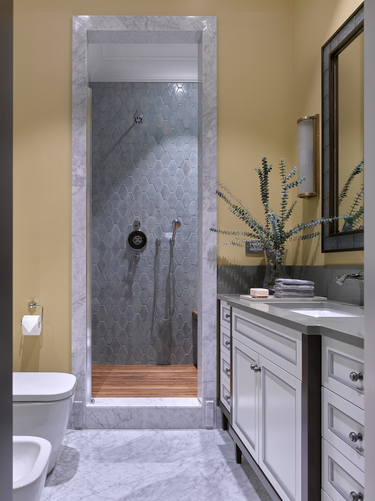 Klassisk inredning av ett mellanstort badrum med dusch, med vita skåp, en dusch i en alkov, en bidé, keramikplattor, gula väggar, marmorgolv, bänkskiva i kvarts, dusch med gångjärnsdörr, luckor med infälld panel, grå kakel, ett undermonterad handfat och grått golv