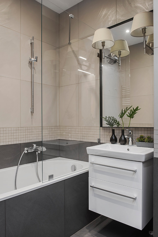 Cette photo montre une salle de bain principale tendance avec des carreaux de porcelaine, un sol en carrelage de porcelaine, un placard à porte plane, des portes de placard blanches, un combiné douche/baignoire, un carrelage beige, un carrelage gris, une baignoire posée et un sol gris.