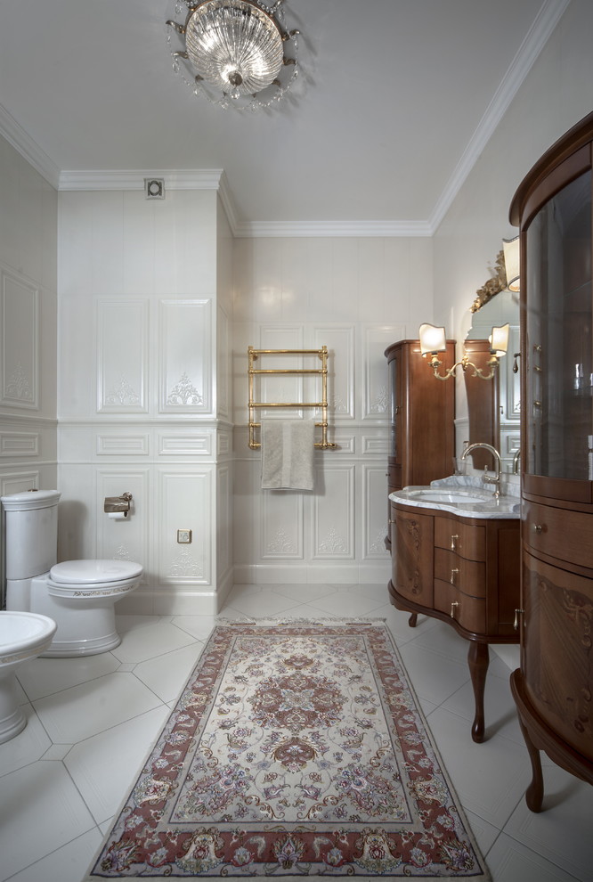 Cette image montre une salle de bain victorienne en bois foncé avec un carrelage blanc, un plan de toilette en marbre, WC séparés, un lavabo encastré, un mur beige et un placard à porte plane.