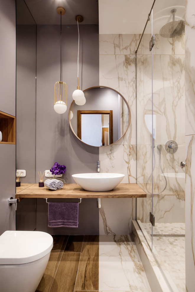 Foto på ett mellanstort funkis brun badrum med dusch, med en vägghängd toalettstol, dusch med gångjärnsdörr, en dusch i en alkov, beige kakel, grå väggar, ett fristående handfat, träbänkskiva och brunt golv