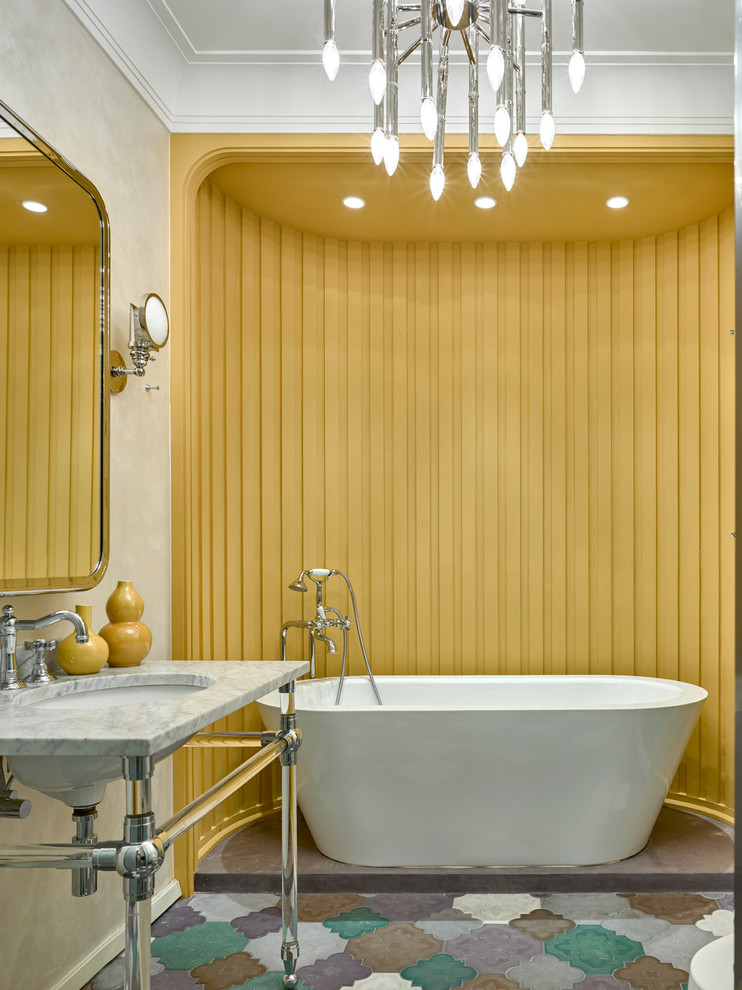 Стильный дизайн: главная ванная комната в стиле неоклассика (современная классика) с отдельно стоящей ванной, разноцветной плиткой, желтыми стенами, консольной раковиной, мраморной столешницей, разноцветным полом, открытыми фасадами и серой столешницей - последний тренд