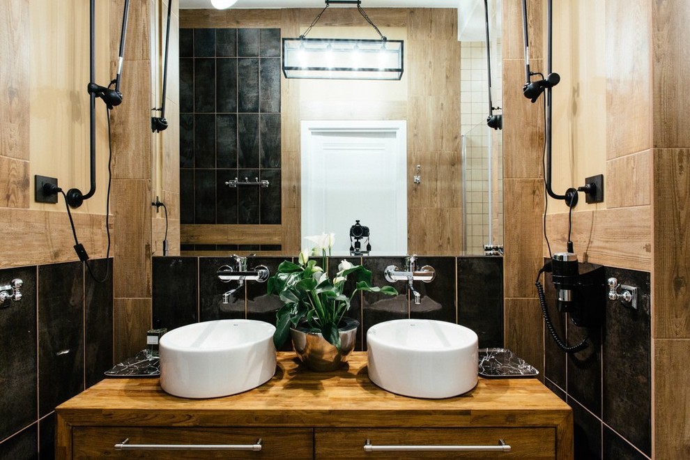 Modelo de cuarto de baño actual de tamaño medio con baldosas y/o azulejos negros, aseo y ducha, encimera de madera y lavabo sobreencimera