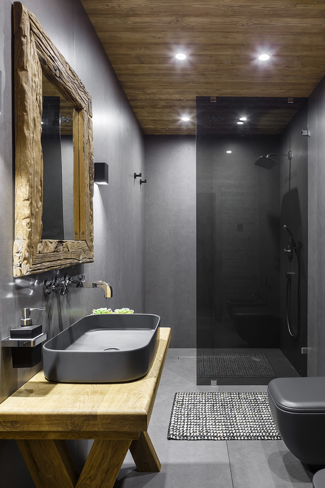 Diseño de cuarto de baño rural con ducha a ras de suelo, paredes grises, aseo y ducha, lavabo sobreencimera, encimera de madera, suelo gris y encimeras marrones