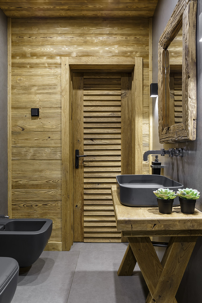 Immagine di una stanza da bagno stile rurale con bidè, pareti grigie, lavabo a bacinella, top in legno e pavimento grigio