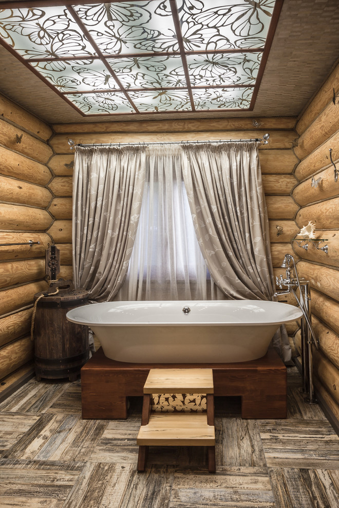 На фото: ванная комната в деревянном доме в стиле рустика с ванной на ножках и полом из керамической плитки