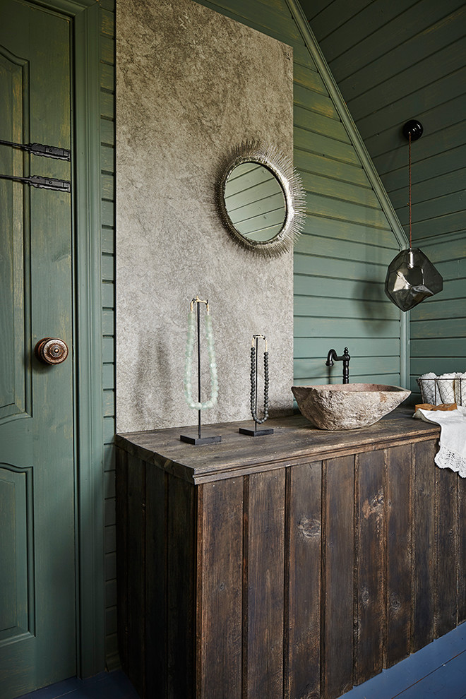 Modelo de cuarto de baño campestre con puertas de armario de madera en tonos medios, paredes verdes, lavabo sobreencimera, suelo azul, armarios con paneles lisos y espejo con luz