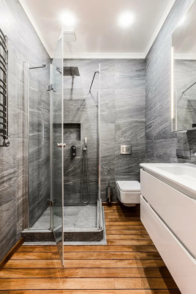 Idée de décoration pour une salle de bain design avec un placard à porte plane, des portes de placard blanches, une douche d'angle, un carrelage gris, un sol en bois brun, un lavabo intégré, un sol marron, une cabine de douche à porte battante et meuble-lavabo suspendu.
