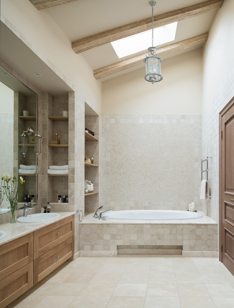 Klassisk inredning av ett en-suite badrum, med luckor med infälld panel, skåp i mellenmörkt trä, ett platsbyggt badkar, beige kakel, travertinkakel, beige väggar, travertin golv, ett nedsänkt handfat och beiget golv