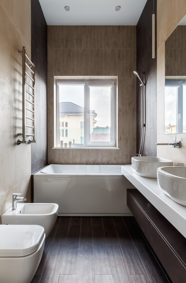 Exempel på ett litet modernt vit vitt en-suite badrum, med släta luckor, skåp i mörkt trä, ett badkar i en alkov, en bidé, beige kakel, porslinskakel, klinkergolv i porslin, bänkskiva i kvarts, brunt golv och ett fristående handfat