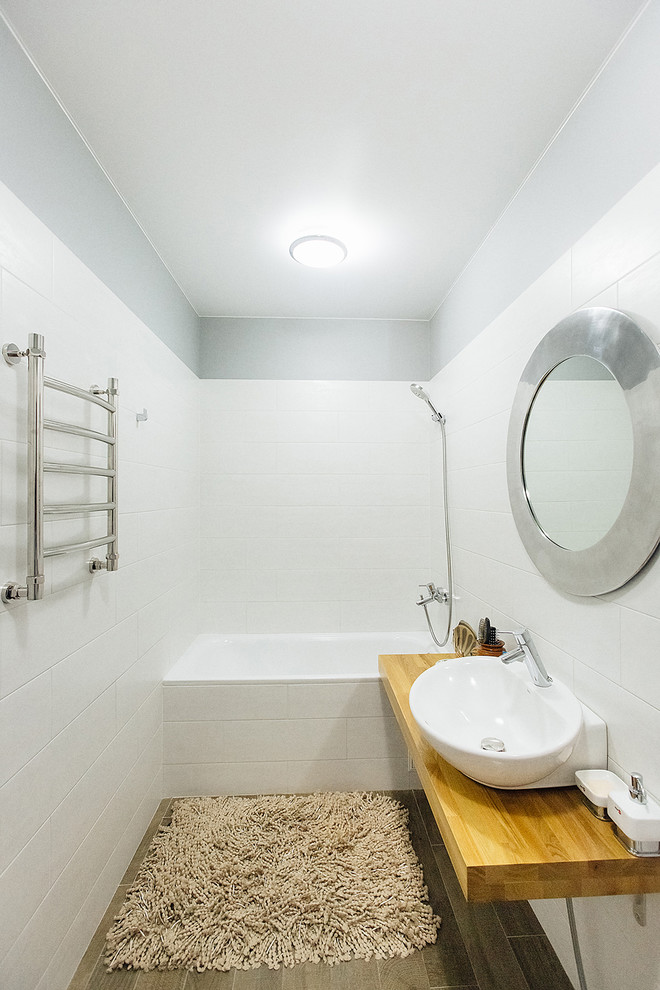 Идея дизайна: маленькая ванная комната в скандинавском стиле с ванной в нише, душем над ванной, белой плиткой, керамической плиткой, серыми стенами, полом из керамогранита, накладной раковиной, столешницей из дерева и серым полом для на участке и в саду