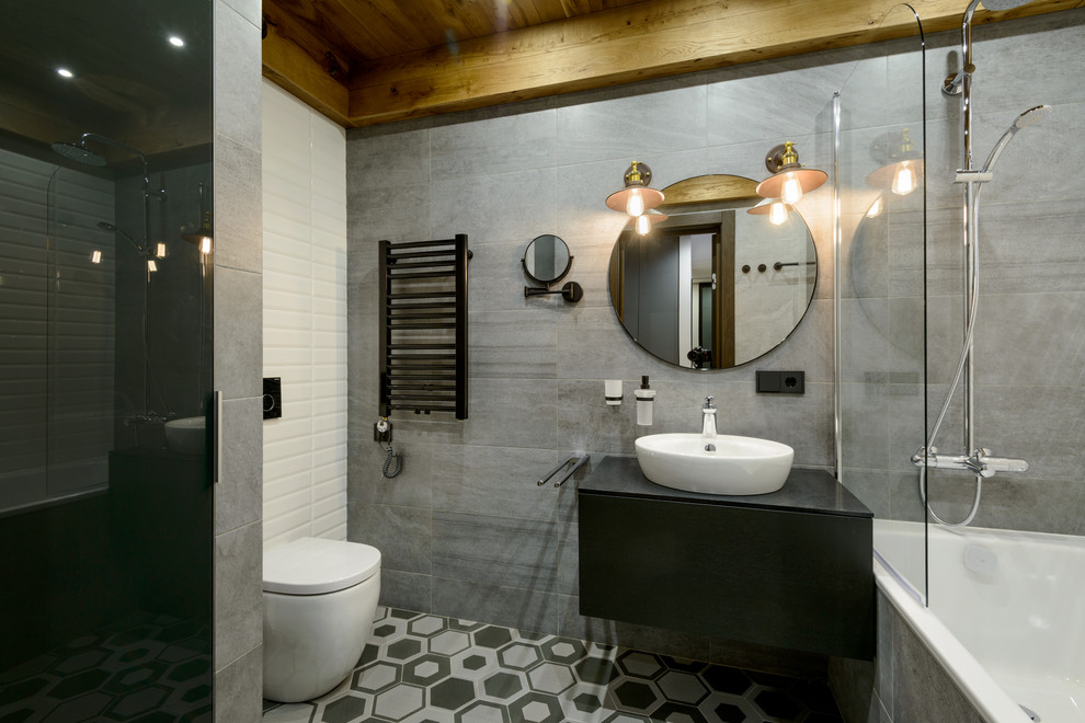 Идея дизайна: ванная комната в стиле лофт с плоскими фасадами, черными фасадами, ванной в нише, душем над ванной, унитазом-моноблоком, серой плиткой, серыми стенами, душевой кабиной, настольной раковиной, серым полом, открытым душем и черной столешницей