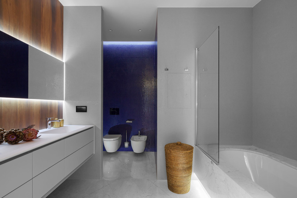 Пример оригинального дизайна: главная ванная комната в современном стиле с плоскими фасадами, белыми фасадами, ванной в нише, инсталляцией, синей плиткой, белой плиткой, плиткой мозаикой, монолитной раковиной и серым полом
